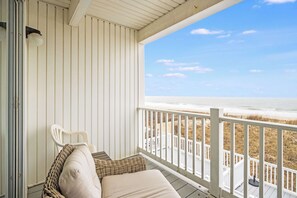 Een overdekte veranda met uitzicht op het strand, een witte stoel en een met kussens uitgeruste bank.
