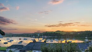 A marina with boats docked, a calm water body, and a hilly landscape in the background.