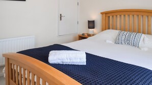 A neatly made bed with a blue blanket and a white towel, a wooden headboard, a bedside lamp, and a framed picture on the wall.