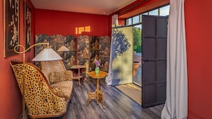 A room with a red wall, a leopard print chair, a small round table with a vase, and a large window with a view of greenery.