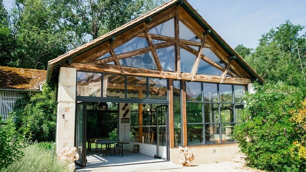 A modern glass conservatory with a wooden frame, a bench, and a table outside. - Moulin Des Libellules (Parcoul)