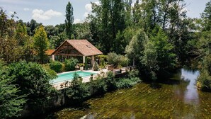 A house with a swimming pool surrounded by lush greenery and a river. - Moulin Des Libellules (Parcoul)