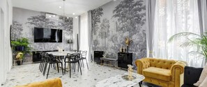 Una sala de estar moderna con una mesa de comedor redonda, sillas negras, un sofá amarillo y un televisor montado en la pared.