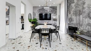 Un comedor moderno con una mesa redonda, sillas negras, una araña y un mural temático de bosque.