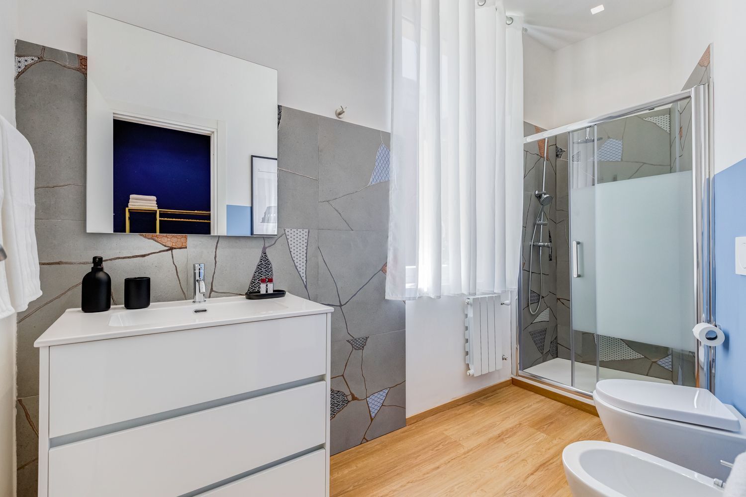 Un bagno moderno con un mobile lavabo bianco, cabina doccia in vetro e parete azzurra.