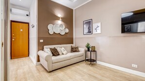 A modern living room with a beige sofa, a small side table, and a wall-mounted light fixture.