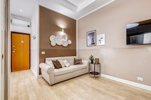 Una sala de estar con un sofá color beige, una mesita auxiliar y un aplique de pared.