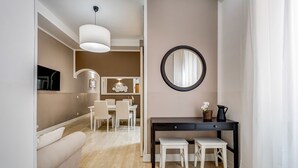 A modern living room with a sofa, a dining area with a table and chairs, a black console table with a mirror, and a light fixture.