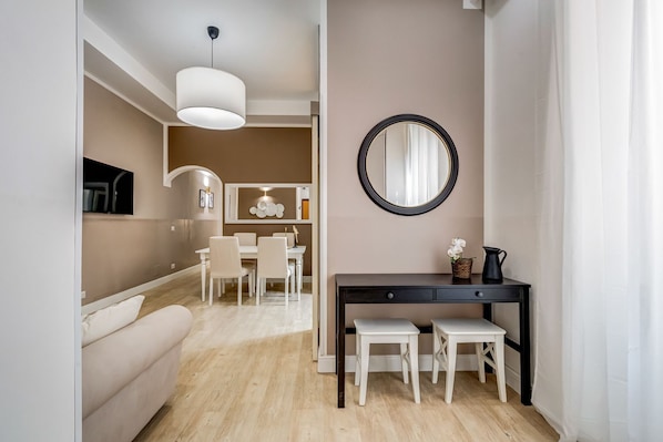 Una sala de estar moderna con un sofá, un comedor con una mesa y sillas, un aparador negro con un espejo, y una lámpara.