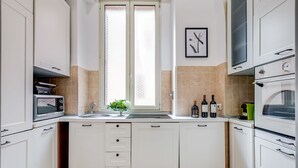 A modern kitchen with white cabinets, a built-in oven, a microwave, and a window with a view.