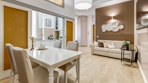A modern living room with a dining area, featuring a white table, beige sofa, and a decorative wall with circular patterns.