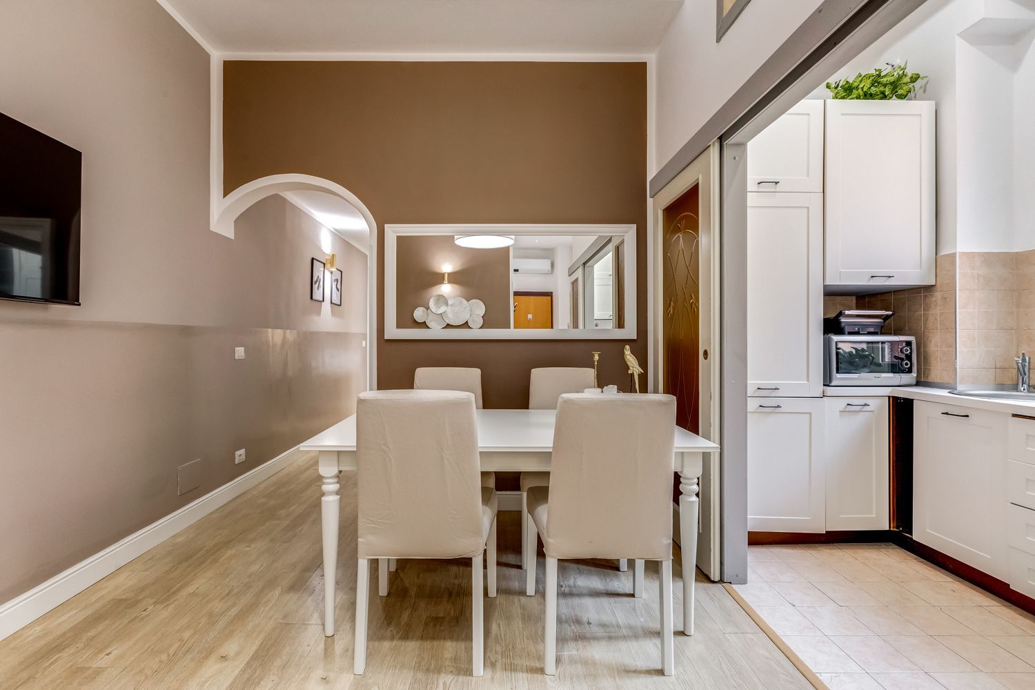 Una cucina moderna con mobili bianchi, un'area pranzo con tavolo e sedie bianche, e un microonde in vista.
