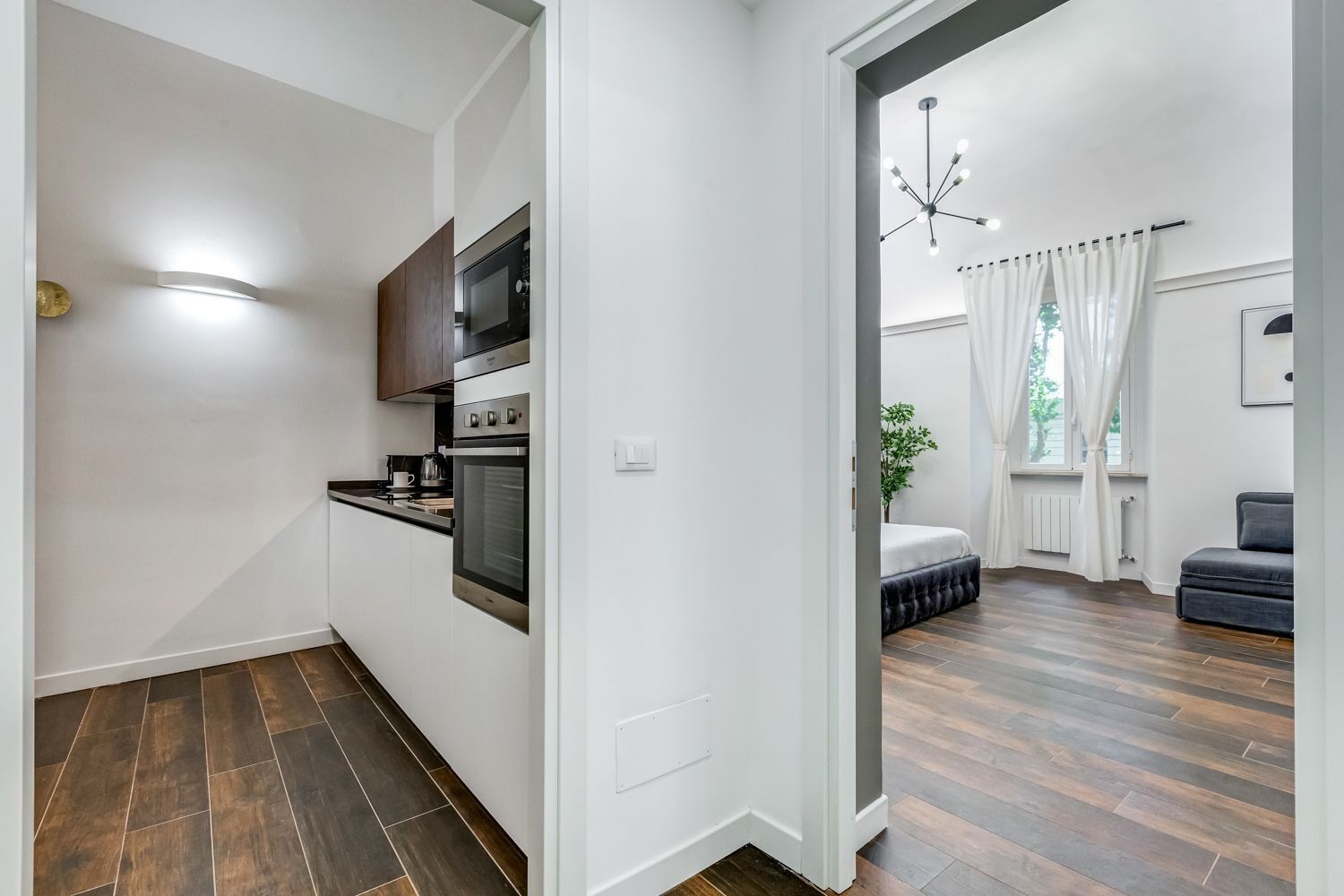 Una cocina moderna con electrodomésticos integrados, un comedor con un sofá de color oscuro y vistas al exterior a través de una ventana.