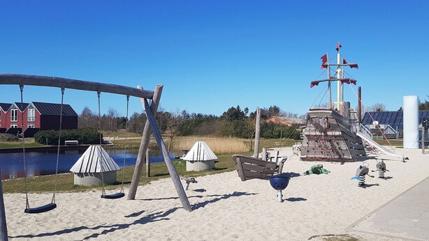 Une aire de jeux avec des balançoires, une structure d’escalade et un petit modèle de bateau.