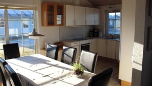 Une cuisine compacte avec des meubles blancs, une table à manger avec des chaises et une vue sur l’extérieur grâce à de grandes fenêtres.