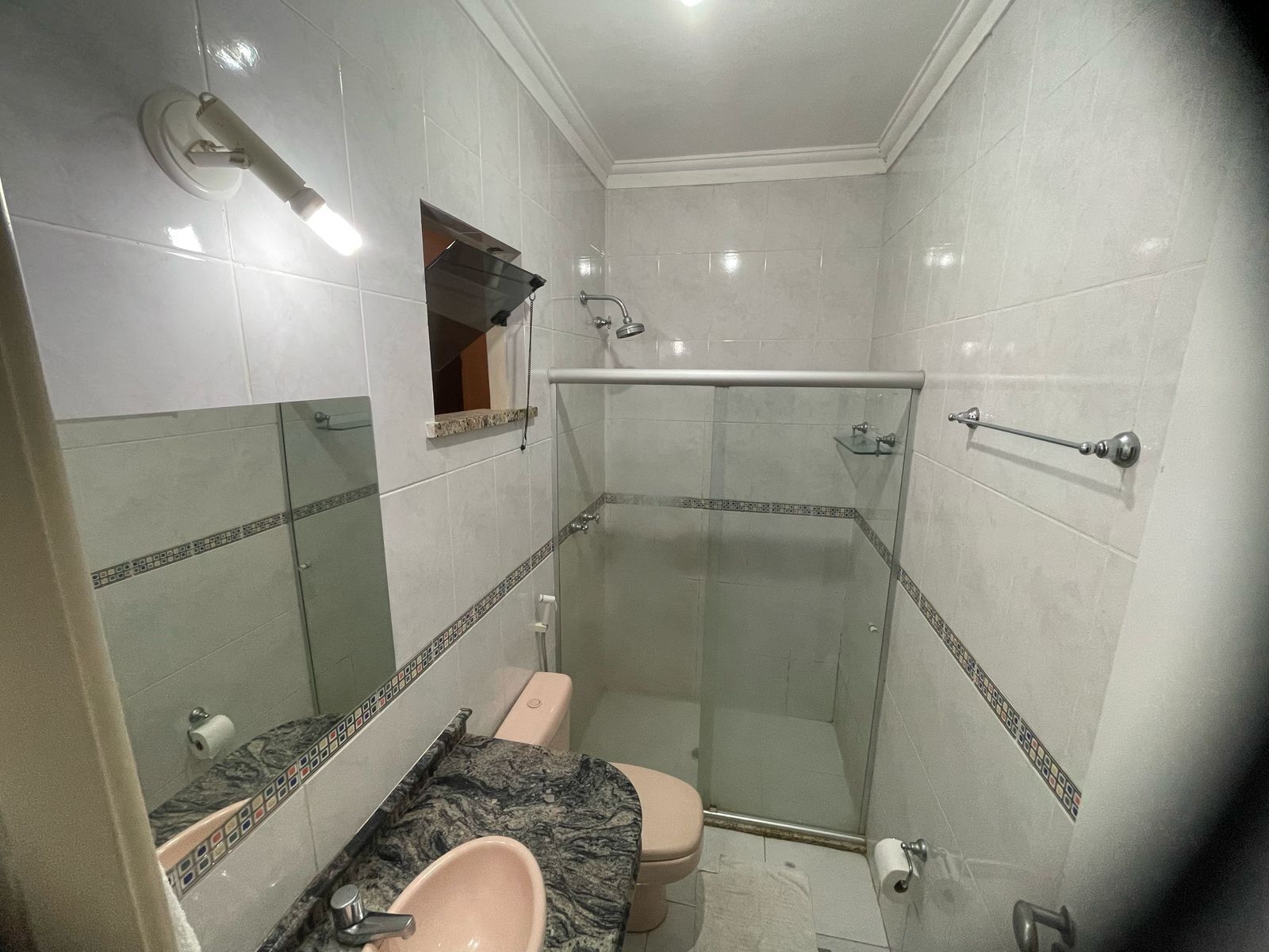 A bathroom with a glass-enclosed shower, a marble sink, and a toilet.