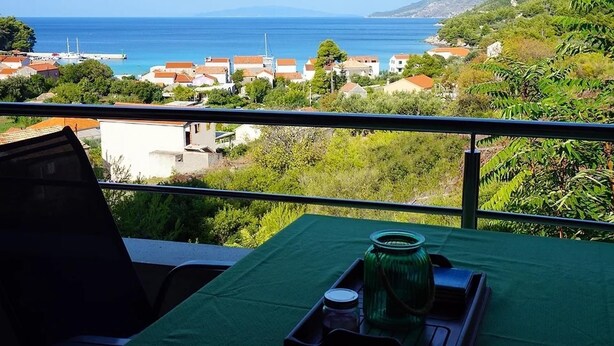 A balcony with a table set for two, overlooking a coastal town with houses and the sea. - Marinero-sea Breeze Escape in Zuljana (Ston)