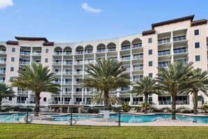 A multi-story hotel with a swimming pool and palm trees.