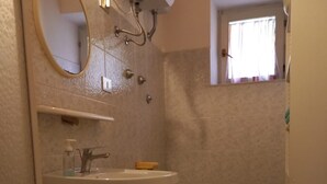 Un baño con lavamanos pedestal, dos inodoros, un espejo y una ventana con cortinas.