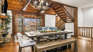 Amplia sala de estar con escalera de madera, una gran mesa de comedor y un rincón de estar acogedor.