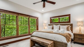 Un dormitorio con un ventanal grande, una cama, un banco y un ventilador de techo.