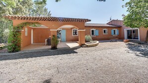 A building with a tiled roof, a gravel driveway, and a small garden area with a bench and potted plants.