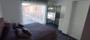 A bedroom with a bed, a nightstand, a lamp, a window with curtains, and a door.