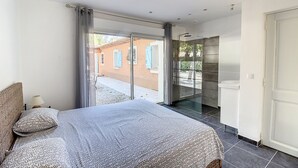 A bedroom with a bed, a nightstand, a window with curtains, and a view of the outside.