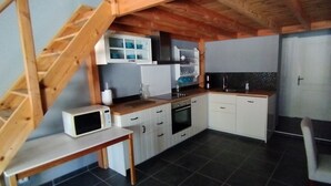 A compact kitchen with white cabinets, a microwave, and a wooden staircase.