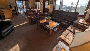A spacious living room with a large window, a fireplace, and a cozy seating area. - Cedar & Sky Retreat- Rustic Lakeview Cabin (Bigfork)