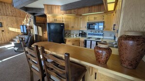 A kitchen with wooden cabinets, a black refrigerator, a stove, and a large vase on the counter. - Cedar & Sky Retreat- Rustic Lakeview Cabin (Bigfork)