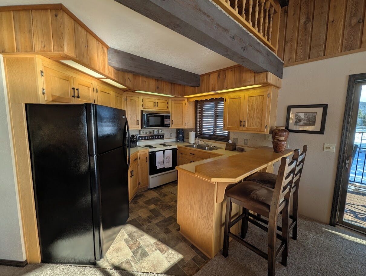 Une cuisine avec des meubles de rangement en bois, un réfrigérateur noir, une cuisinière et un évier.