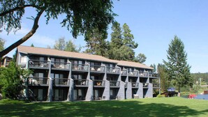 Un immeuble à plusieurs étages doté de balcons, entouré d’une zone verdoyante et d’arbres.