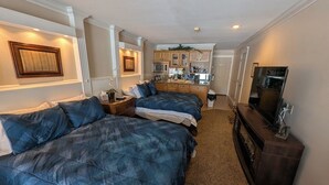Une chambre d’hôtel avec deux lits, une télévision, un bureau et, au fond, une kitchenette.