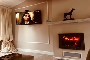 Una sala de estar con un televisor montado en la pared, una chimenea y una figura decorativa de un caballo en un estante.