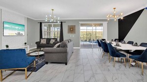 A modern living room with a grey sofa, blue chairs, and a dining area with a white table and blue chairs. - 180 Degree Water Views. No rear Neighbours. Games Rm. Spa. Cinema Star Wars. (Kissimmee)