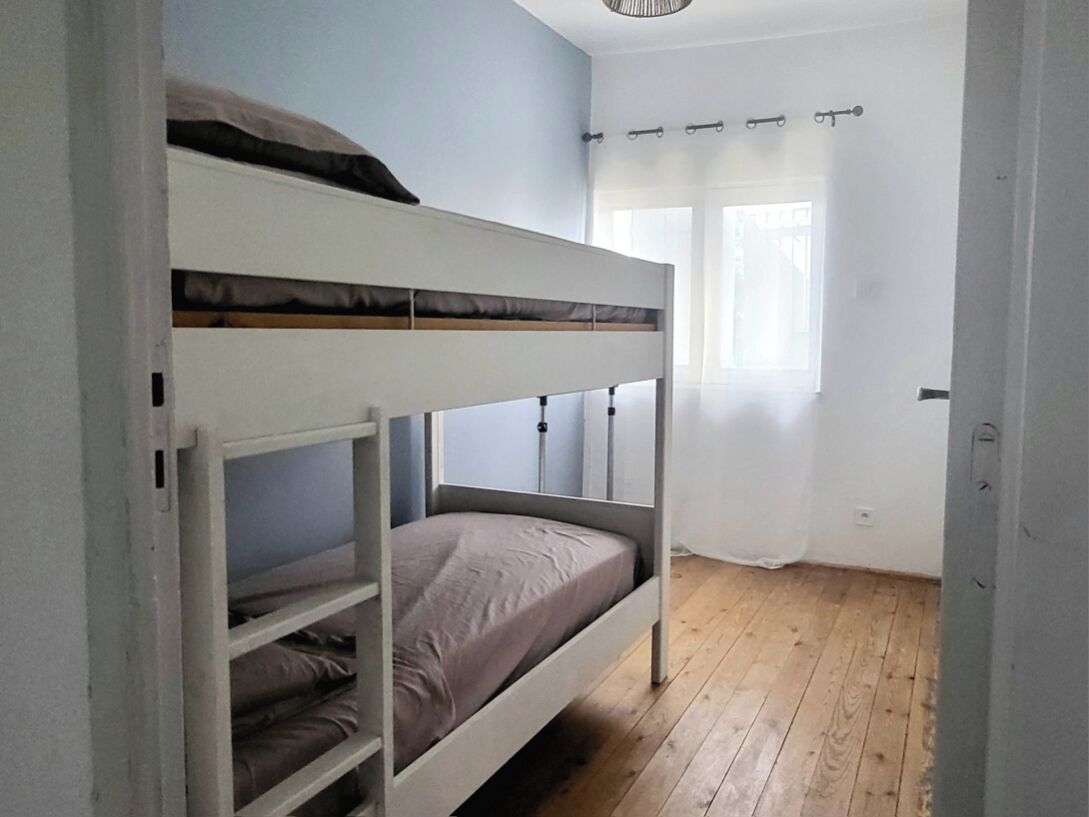 A bunk bed room with a wooden floor, a window with curtains, and a white wall.