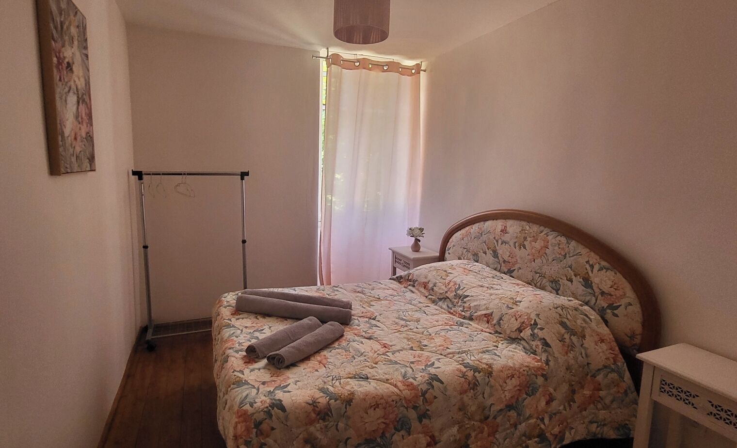 A bedroom with a bed, a nightstand, a window with curtains, and a wall-mounted radiator.