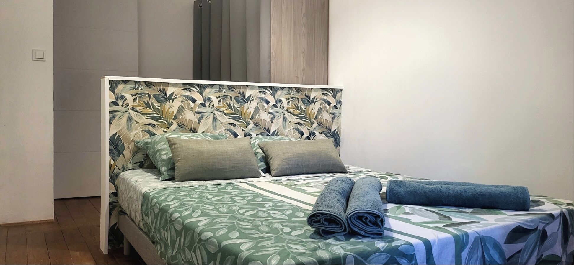 Una cama con cabecera floral, dos almohadas y toallas enrolladas.