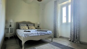 A bedroom with a bed, two bedside tables, a nightstand, a window with curtains, and a door.