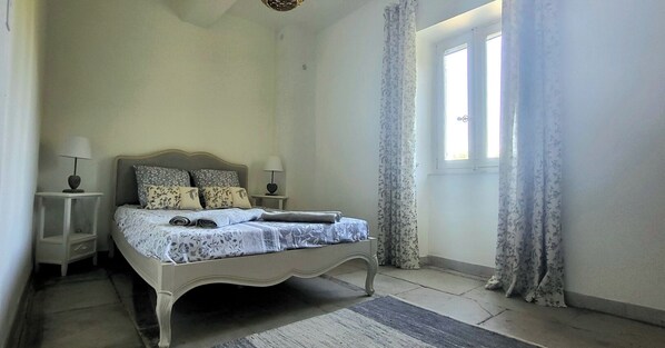 A bedroom with a bed, two bedside tables, a nightstand, a window with curtains, and a door.