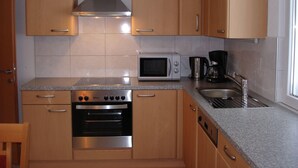 A compact kitchen with wooden cabinets, a stainless steel range hood, a built-in oven, a microwave, a coffee maker, and a sink. - Apartment in Gaschurn for 4 People (Gaschurn)