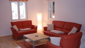 A living room with two red sofas, a coffee table, and a large window with curtains. - Apartment in Gaschurn for 4 People (Gaschurn)