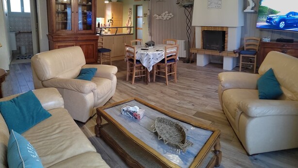 Een woonkamer met een bank, fauteuils, een salontafel en een eethoek met een tafel en stoelen.