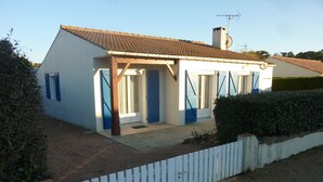Een gelijkvloers huis met een pannendak, een veranda met blauwe luiken en een witte picket-hek.