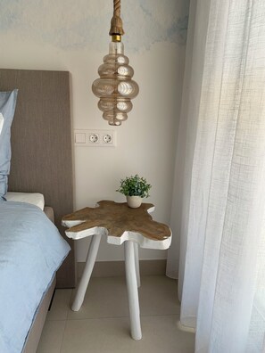 Une chambre à coucher avec un lit, une lampe fixée au mur, une petite table avec une plante et une prise de courant.