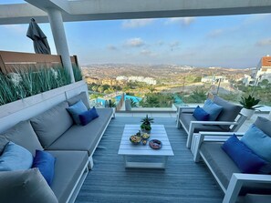 A modern outdoor seating area with a pool view, including a sofa, chairs, and a table with food. - OneHeights: A luxuriously furnished apartment in a prime location with a phenomenal view! (La Cala de Mijas)