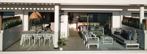 Un espace de repas extérieur moderne, avec des chaises blanches et une table, un coin salon avec des canapés et une table basse, et une plante en pot.