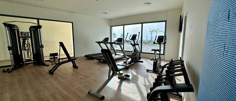 Une salle de sport équipée de divers appareils d’exercice, dotée de grandes fenêtres et d’un plancher en bois.