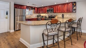Una cocina con armarios de madera, electrodomésticos de acero inoxidable, encimeras de granito y taburetes de bar.
